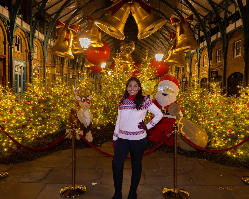 Matty beneath golden Christmas bells among decorated trees inside Covent Garden Market.