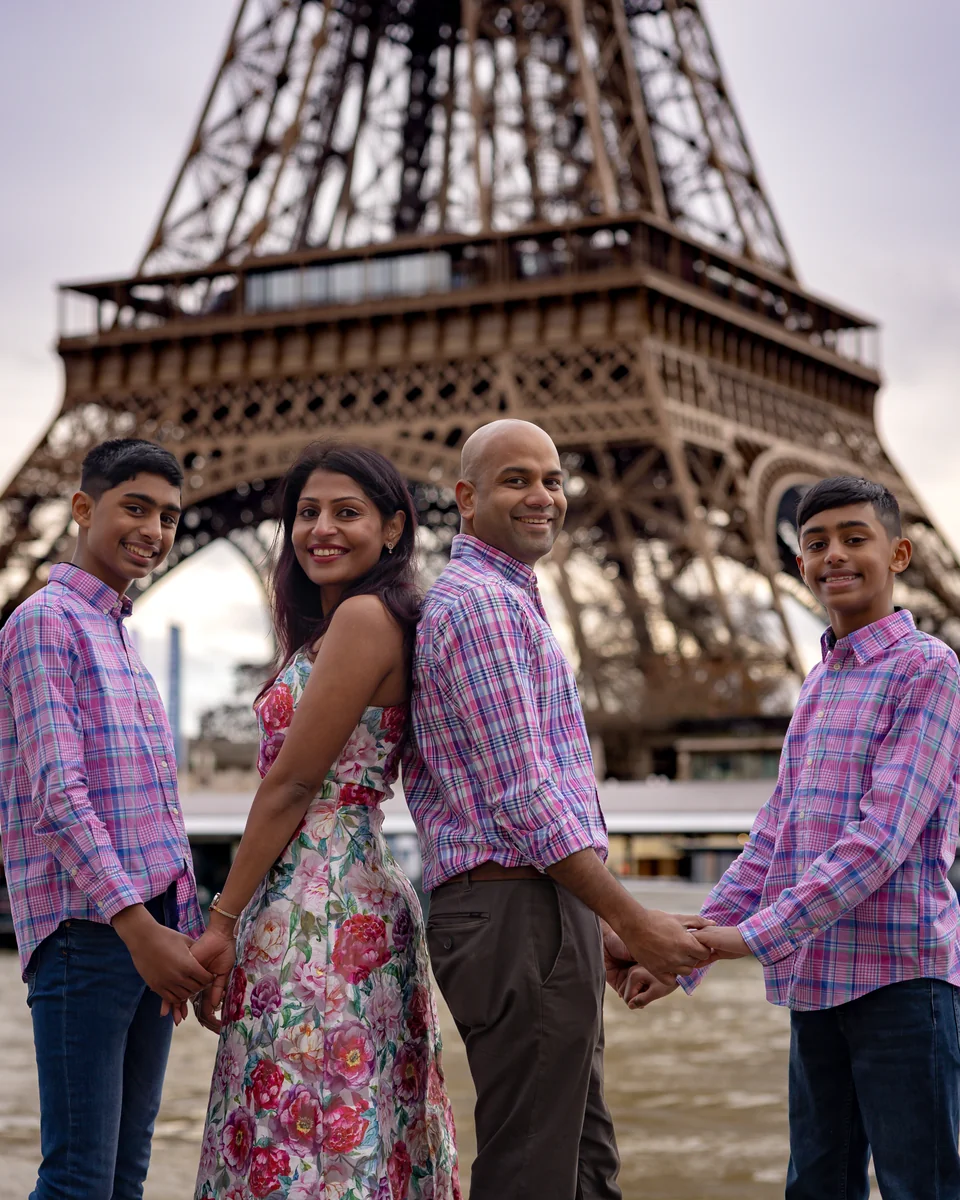Our family of four beneath the Eiffel Tower in Paris, wearing coordinated pink and purple outfits.